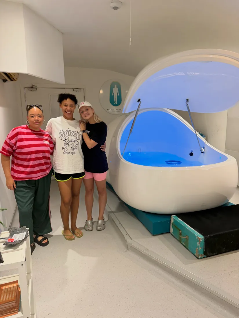 Three smiling guests standing beside an open float pod lit blue.